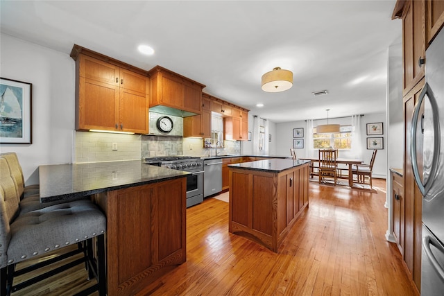 kitchen with light hardwood / wood-style flooring, a breakfast bar area, stainless steel appliances, a center island, and decorative light fixtures