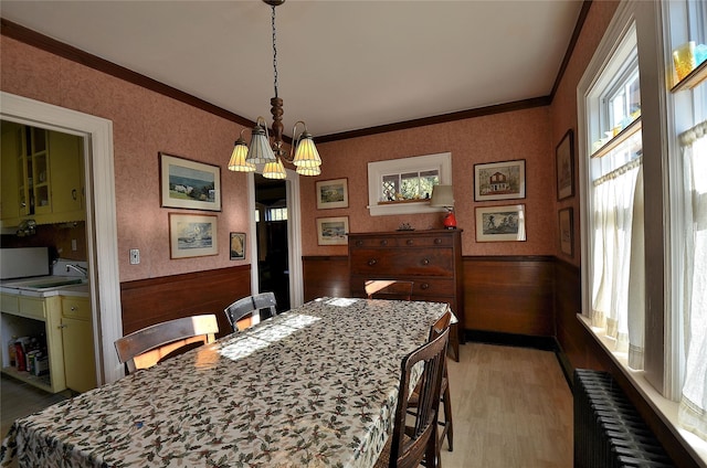 dining space with radiator heating unit, light hardwood / wood-style floors, a chandelier, wooden walls, and ornamental molding