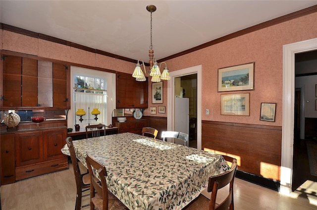 dining room with crown molding, light hardwood / wood-style flooring, wood walls, and a notable chandelier