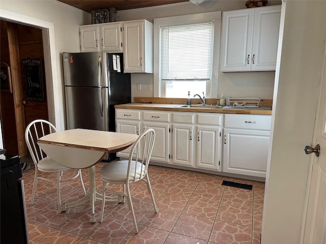 kitchen with stainless steel fridge, white cabinetry, sink, and light tile patterned floors