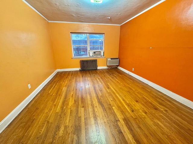 additional living space featuring wood-type flooring, radiator heating unit, a textured ceiling, and a wall mounted air conditioner