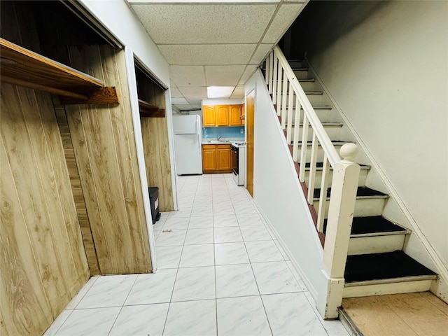 stairway with a drop ceiling, sink, and wood walls