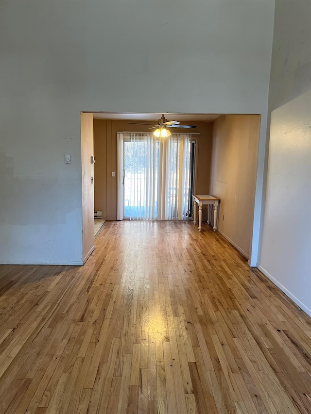 unfurnished living room featuring a towering ceiling, light wood-type flooring, and ceiling fan