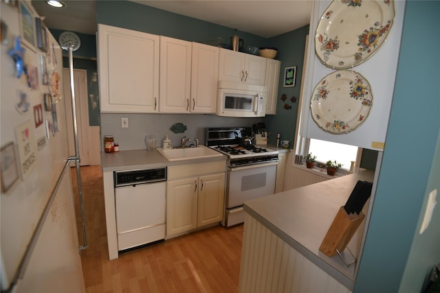 kitchen with white cabinetry, sink, white appliances, and light wood-type flooring