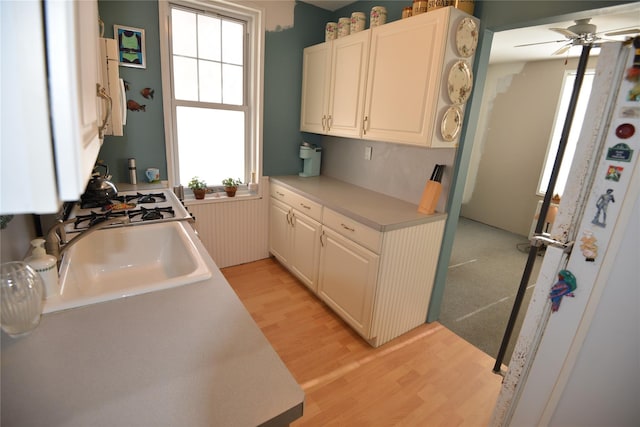 kitchen featuring ceiling fan, white cabinetry, sink, and light hardwood / wood-style flooring