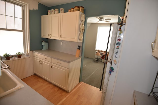 kitchen with white cabinetry, light hardwood / wood-style flooring, ceiling fan, and sink