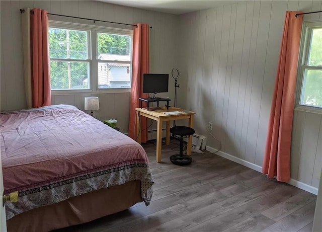 bedroom with baseboard heating, wooden walls, and hardwood / wood-style floors