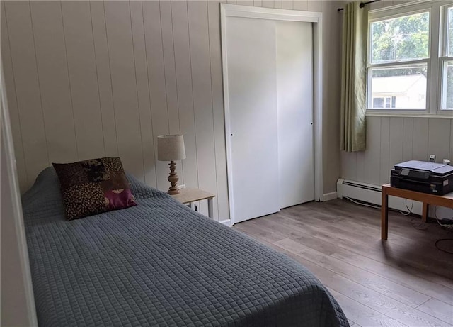 bedroom featuring a baseboard radiator, light hardwood / wood-style flooring, and wooden walls