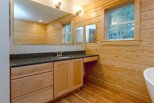 bathroom with wooden walls, hardwood / wood-style floors, vanity, and a bath