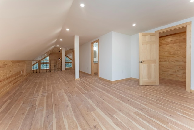 bonus room with light wood-type flooring, lofted ceiling, and wood walls