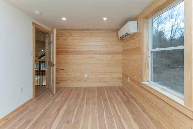 unfurnished room with wood walls, light wood-type flooring, and an AC wall unit