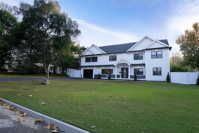 modern farmhouse featuring aphalt driveway, a front yard, an attached garage, and fence