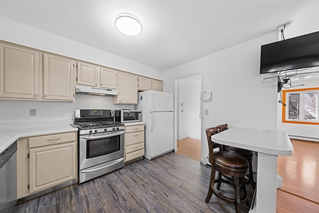 kitchen with a breakfast bar, appliances with stainless steel finishes, cream cabinets, and hardwood / wood-style floors