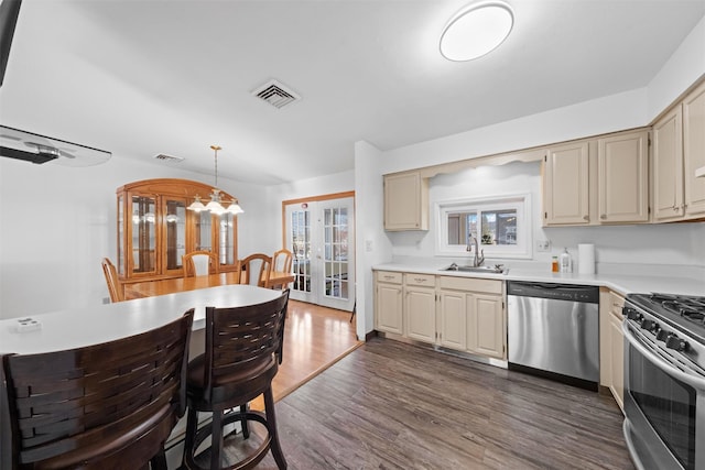 kitchen featuring sink, dark hardwood / wood-style floors, cream cabinets, decorative light fixtures, and appliances with stainless steel finishes