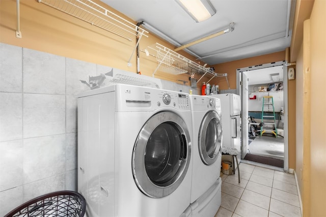 laundry area with light tile patterned floors, independent washer and dryer, and tile walls