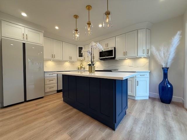 kitchen featuring decorative light fixtures, stainless steel appliances, white cabinetry, and light hardwood / wood-style flooring