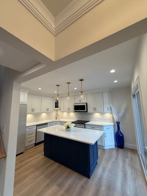 kitchen featuring white cabinets, hanging light fixtures, ornamental molding, appliances with stainless steel finishes, and a kitchen island