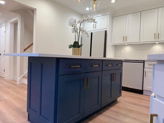 kitchen featuring blue cabinetry, a center island, stainless steel dishwasher, light hardwood / wood-style floors, and white cabinets