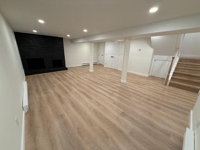 basement featuring a large fireplace, a baseboard heating unit, and light hardwood / wood-style flooring