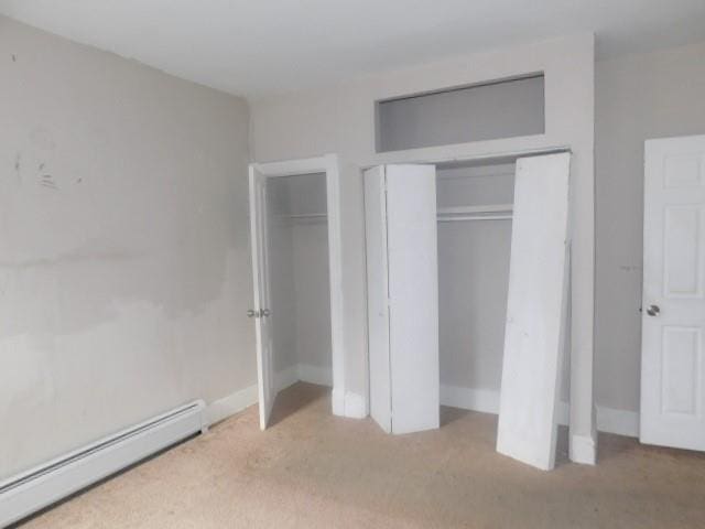 unfurnished bedroom featuring light colored carpet and a baseboard heating unit