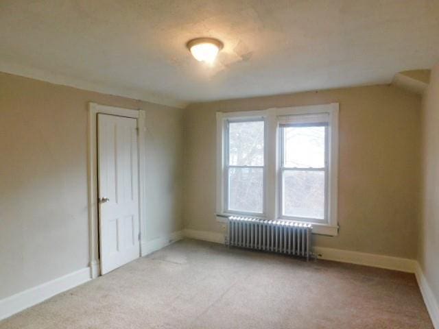 interior space featuring light carpet, radiator heating unit, and vaulted ceiling