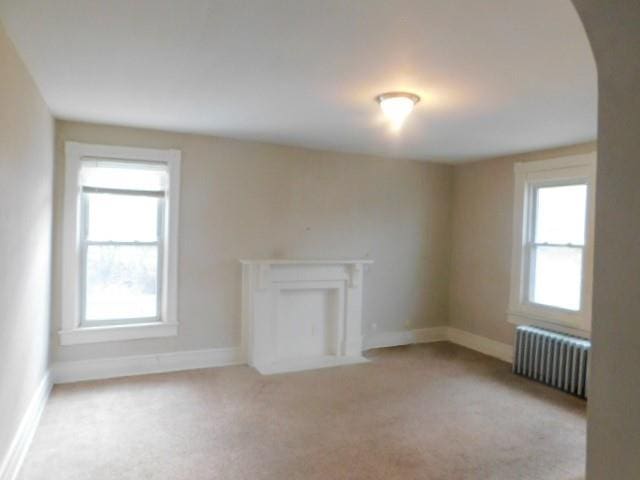 unfurnished living room featuring light colored carpet and radiator