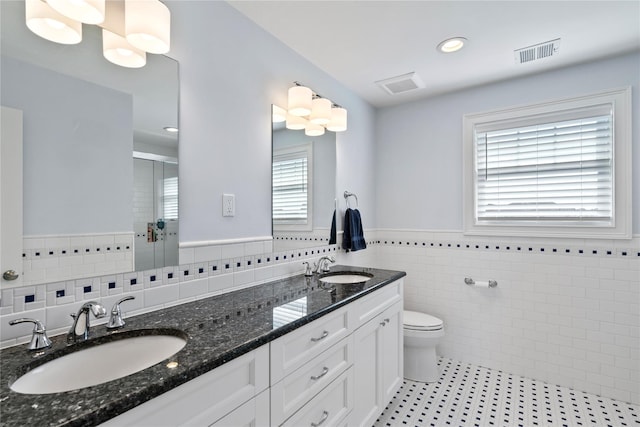 bathroom featuring vanity, a shower with door, tile walls, toilet, and plenty of natural light