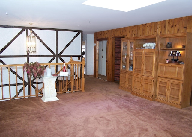 unfurnished living room featuring wooden walls, carpet floors, and an inviting chandelier