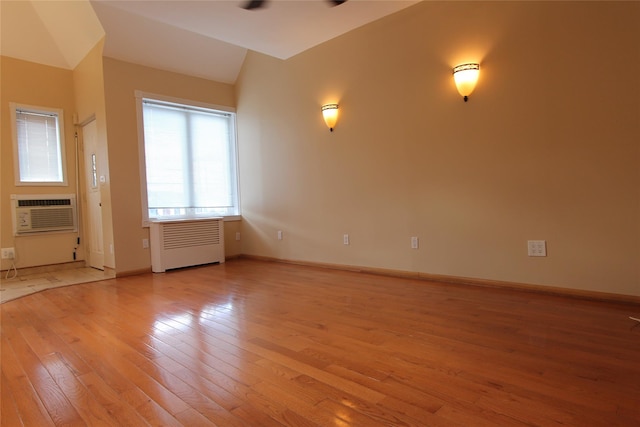 unfurnished room featuring ceiling fan, radiator heating unit, a wall mounted air conditioner, and light wood-type flooring