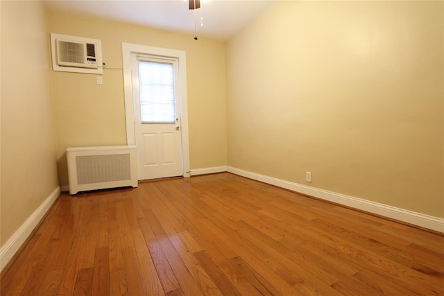 empty room with ceiling fan, wood-type flooring, radiator heating unit, and a wall unit AC