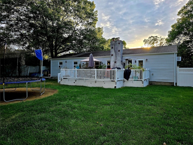 back house at dusk featuring a lawn, a deck, and a trampoline