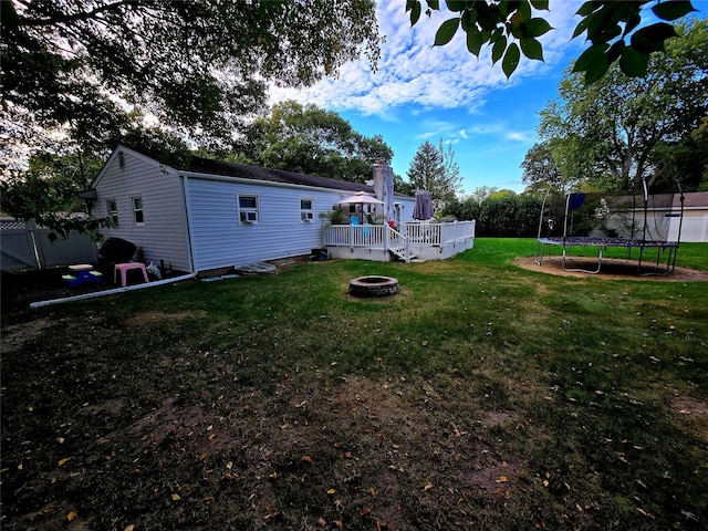 view of yard with a deck, a trampoline, and an outdoor fire pit