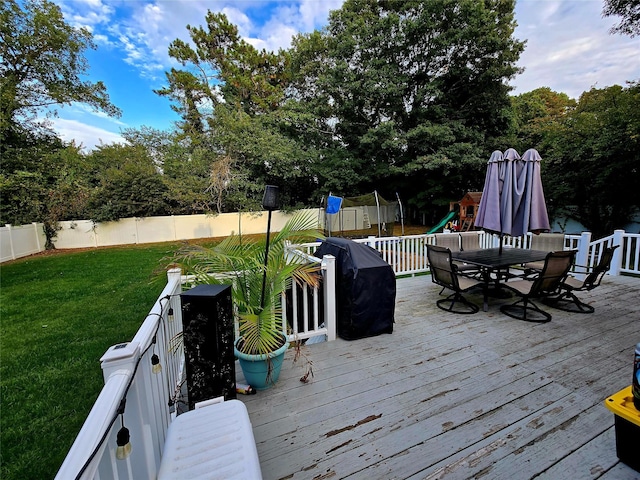 wooden deck featuring a grill, a yard, and a trampoline