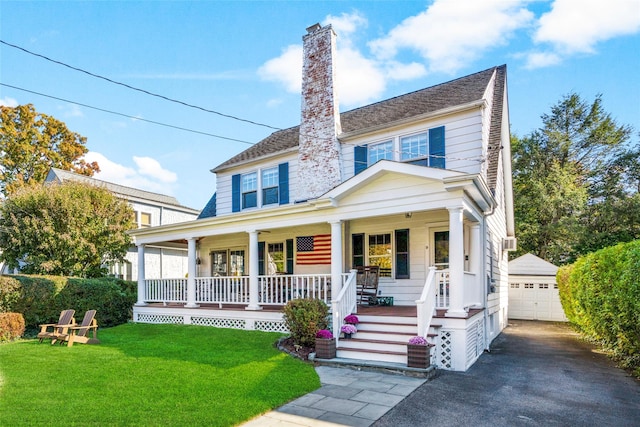 view of front of house featuring an outbuilding, a chimney, covered porch, a front yard, and a garage