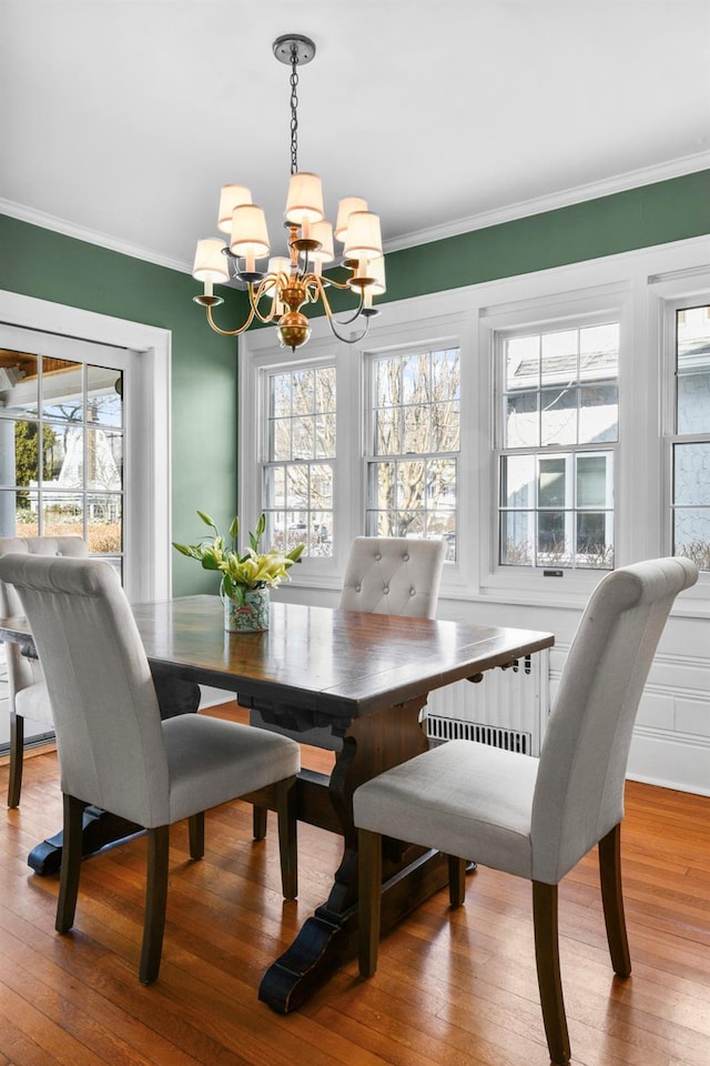 dining space featuring a healthy amount of sunlight, a chandelier, wood finished floors, and ornamental molding