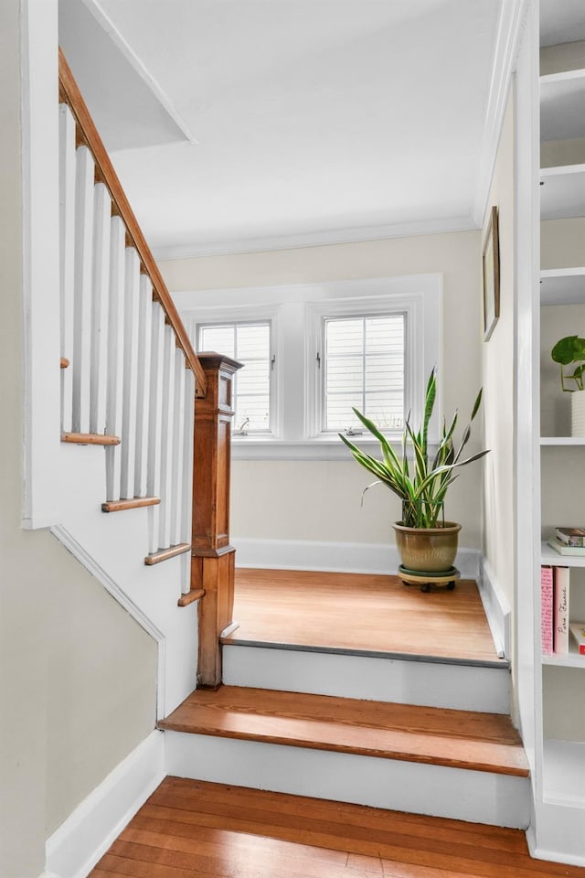 stairway featuring baseboards, wood finished floors, and ornamental molding