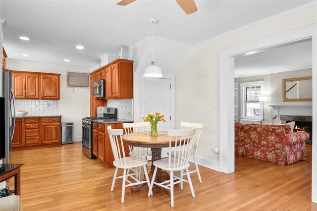 kitchen featuring brown cabinetry, dark stone countertops, hanging light fixtures, stainless steel appliances, and crown molding