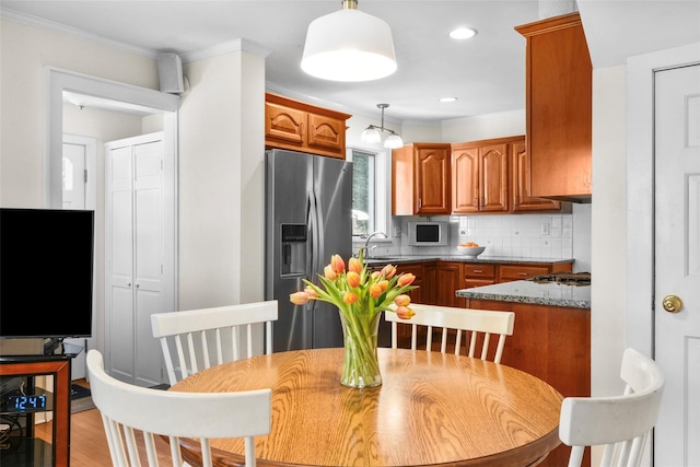 kitchen with tasteful backsplash, stainless steel fridge, brown cabinetry, white microwave, and decorative light fixtures