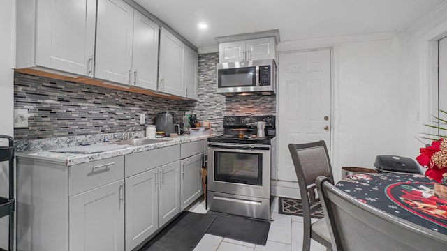 kitchen featuring sink, ornamental molding, appliances with stainless steel finishes, tasteful backsplash, and light tile patterned flooring