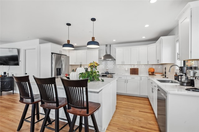 kitchen featuring appliances with stainless steel finishes, wall chimney exhaust hood, pendant lighting, white cabinetry, and a kitchen island