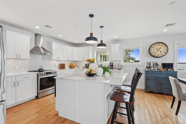 kitchen with white cabinetry, wall chimney range hood, hanging light fixtures, and stainless steel stove