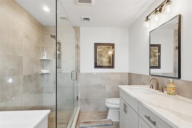 bathroom featuring vanity, toilet, tile walls, and a shower with shower door