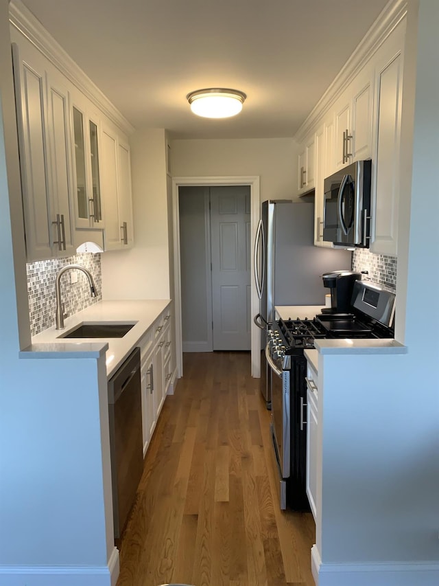 kitchen with sink, stainless steel appliances, wood-type flooring, white cabinets, and decorative backsplash