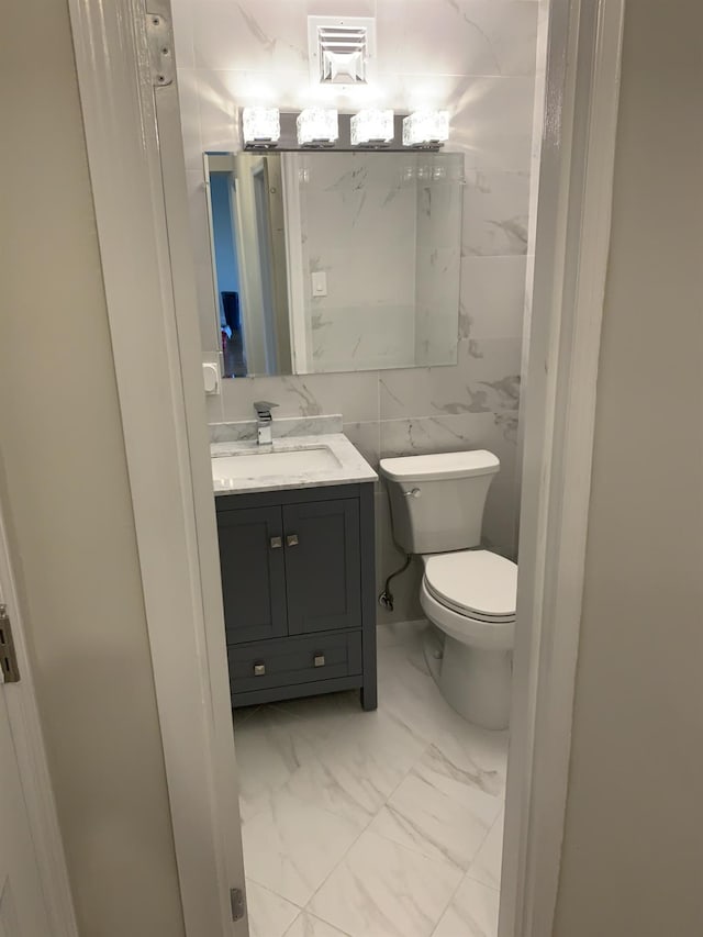 bathroom featuring vanity, tile walls, and toilet