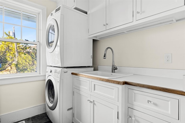 clothes washing area with cabinets, stacked washer and clothes dryer, and sink