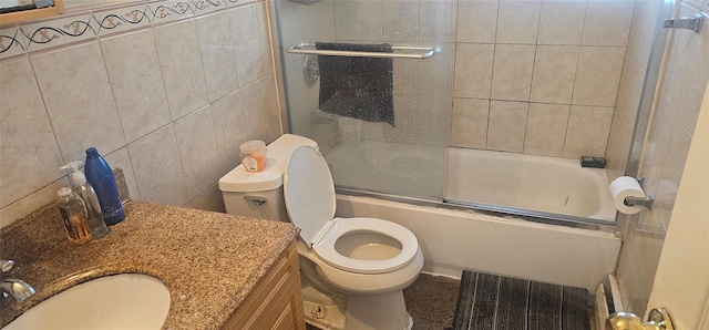 full bathroom featuring vanity, toilet, bath / shower combo with glass door, and tile walls