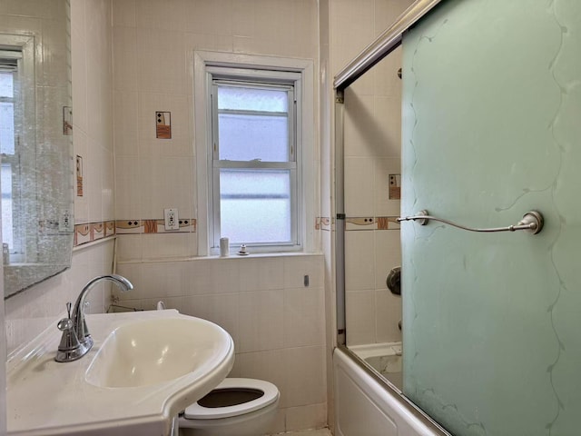 full bathroom with sink, toilet, tile walls, and bath / shower combo with glass door