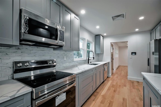 kitchen with stainless steel appliances, light stone counters, and gray cabinetry