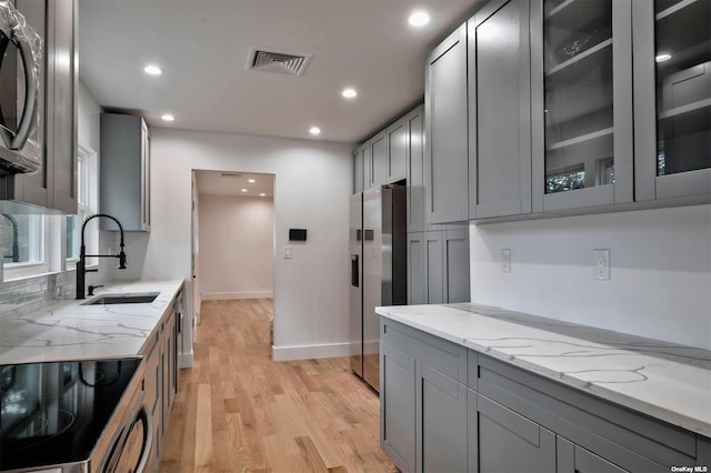 kitchen featuring sink, light stone counters, light hardwood / wood-style flooring, stainless steel refrigerator with ice dispenser, and stove