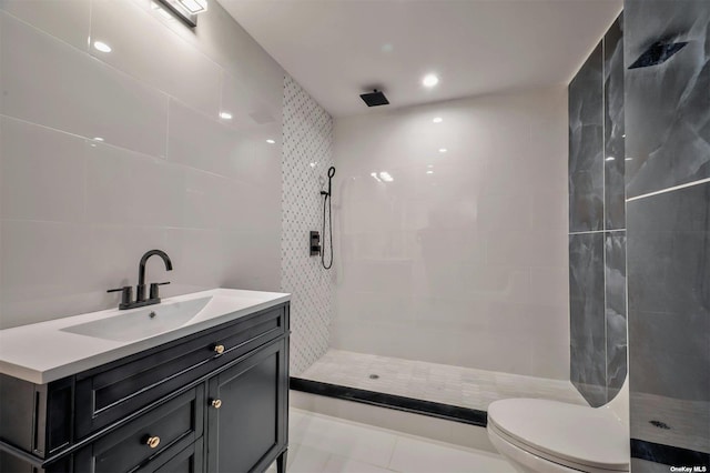 bathroom featuring tile patterned flooring, toilet, tiled shower, vanity, and tile walls